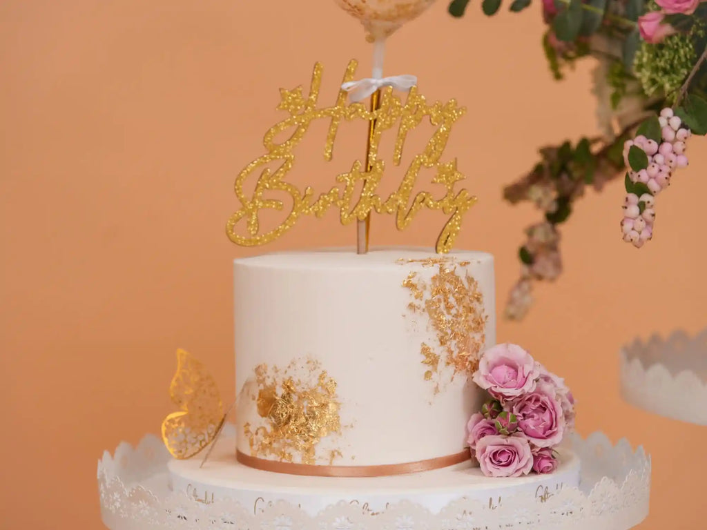 White cake with gold decorations and a 'Happy Birthday' topper on an orange background– thoughtful gift basket for birthdays, anniversaries, and celebrations in Lebanon