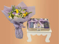 Bouquet of flowers wrapped in purple paper with a small gift set on a stand against a peach background