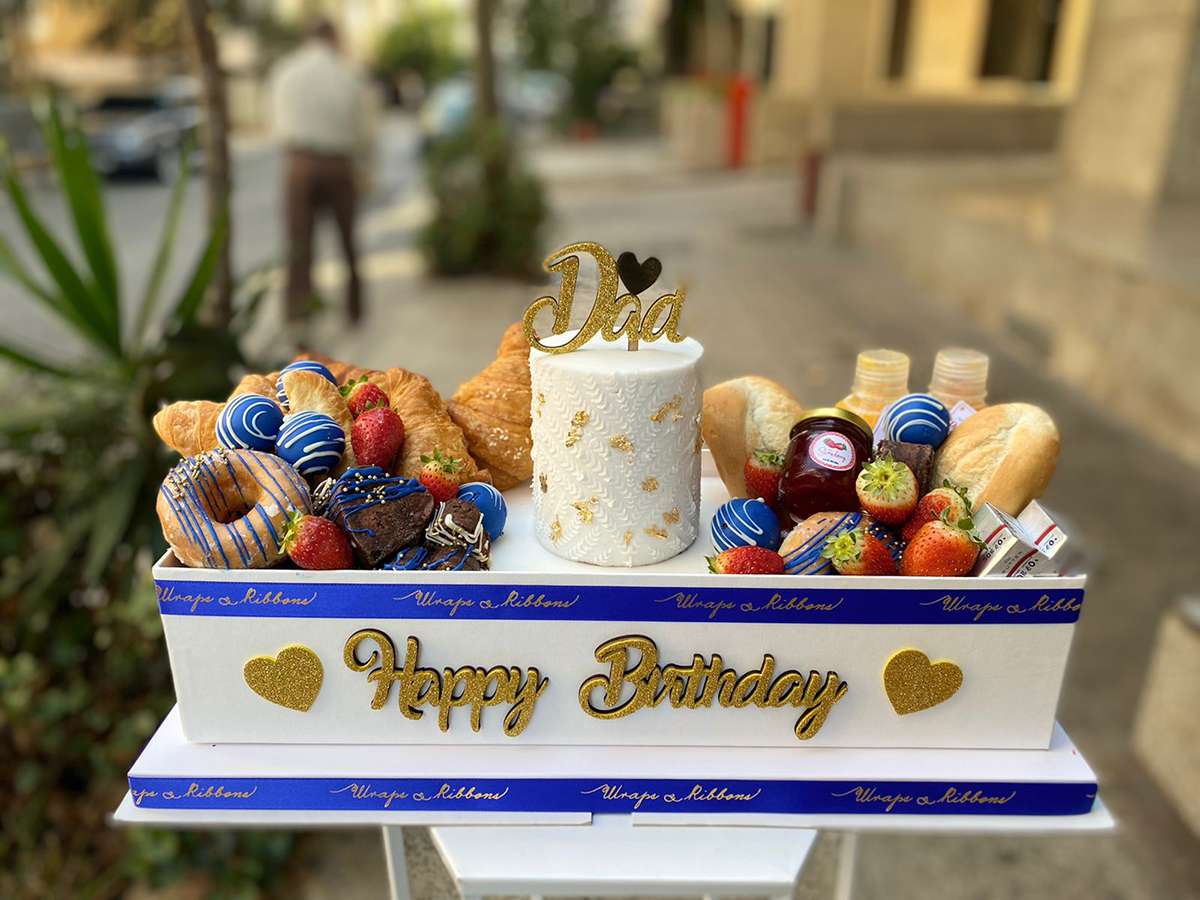 Breakfast box and Birthday cake with various items on a table outdoors
