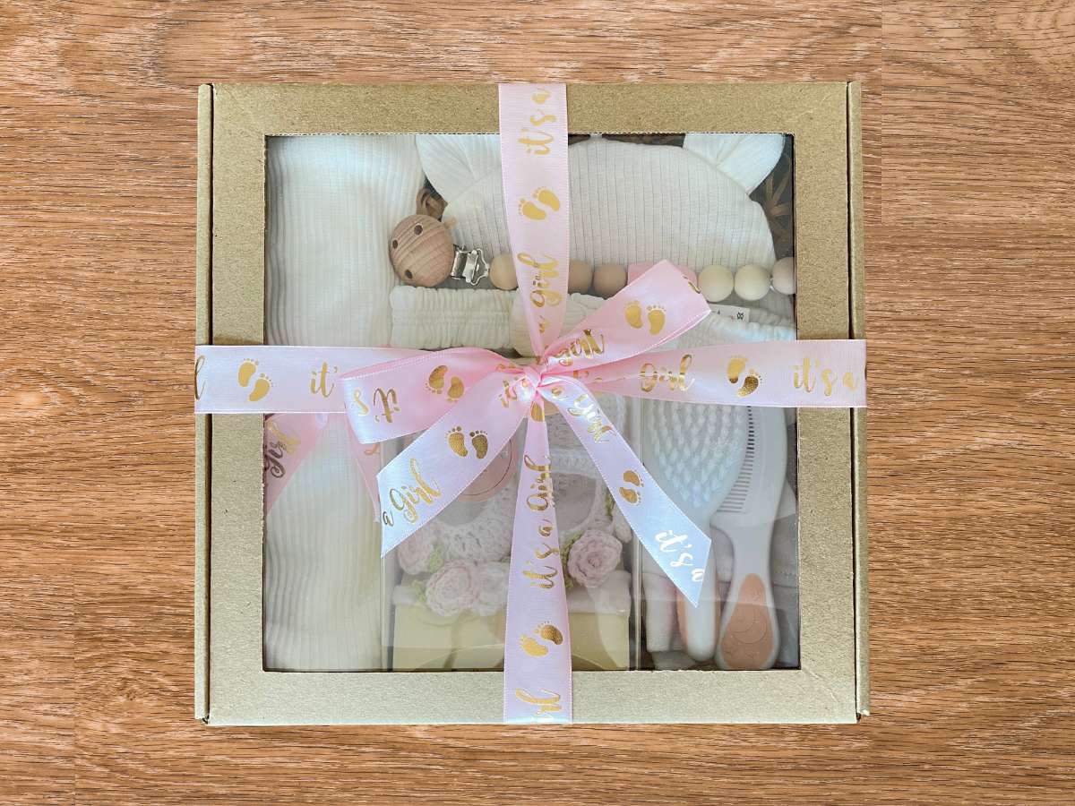 Baby gift set with clothes and a rattle in a box on a wooden surface