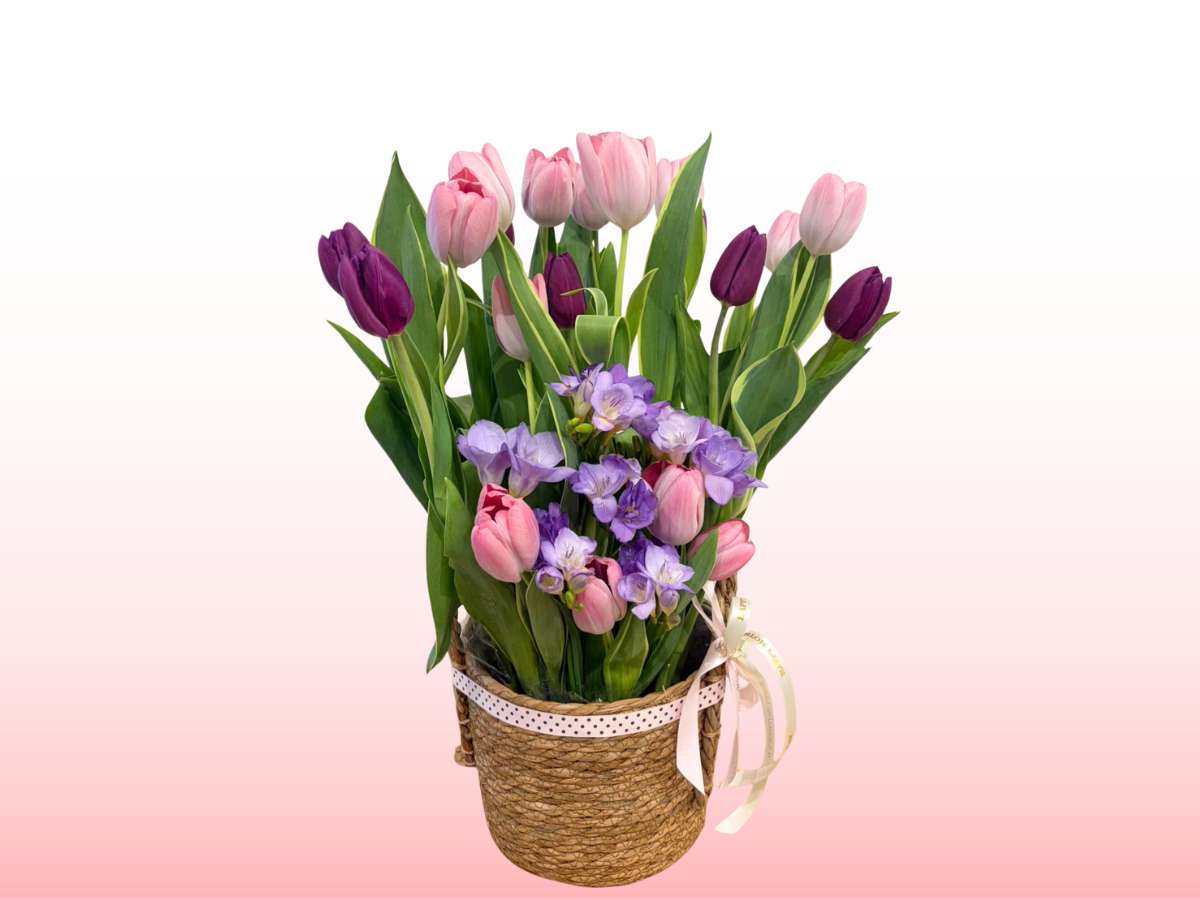 Bouquet of tulips and irises in a woven basket on a pink background