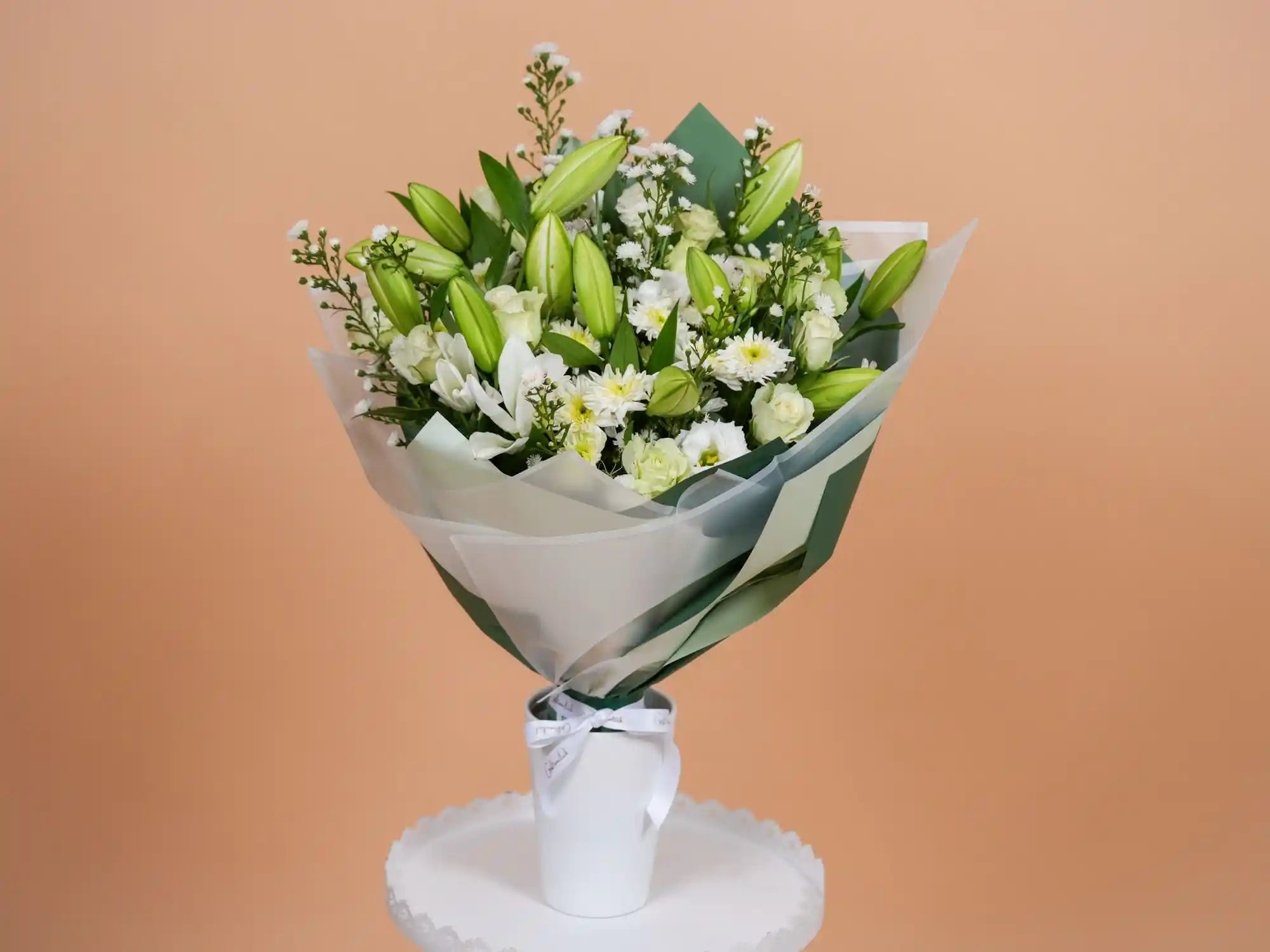 Bouquet of flowers wrapped in white paper on a round white stand with a beige background